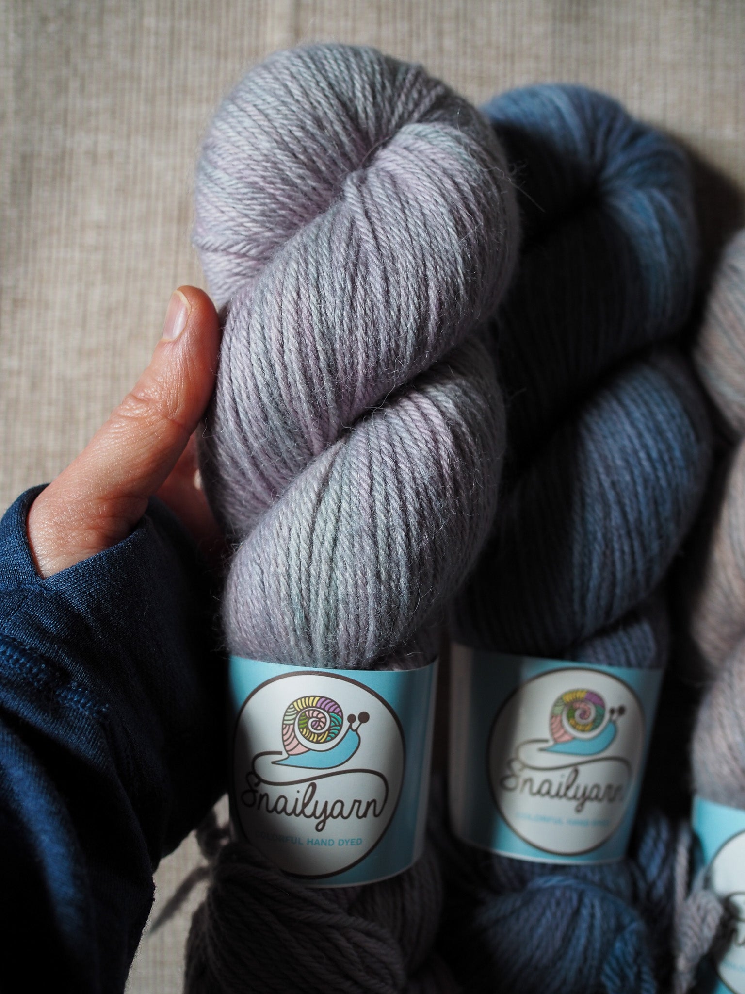 Three skeins of yarn with labels held by a hand on a textured surface