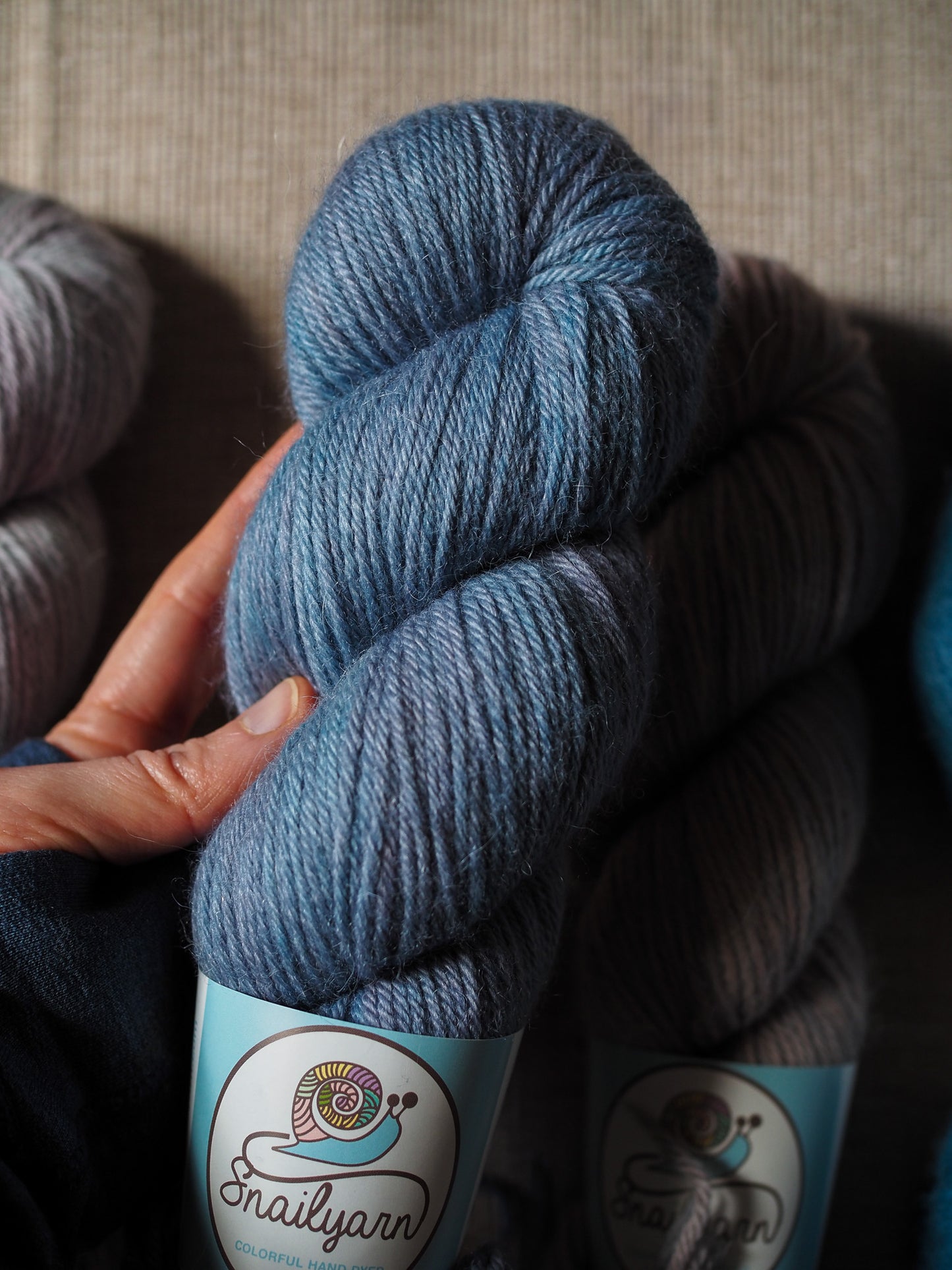 Blue skein of yarn held by a hand with 'Snail Yarn' label on a textured surface