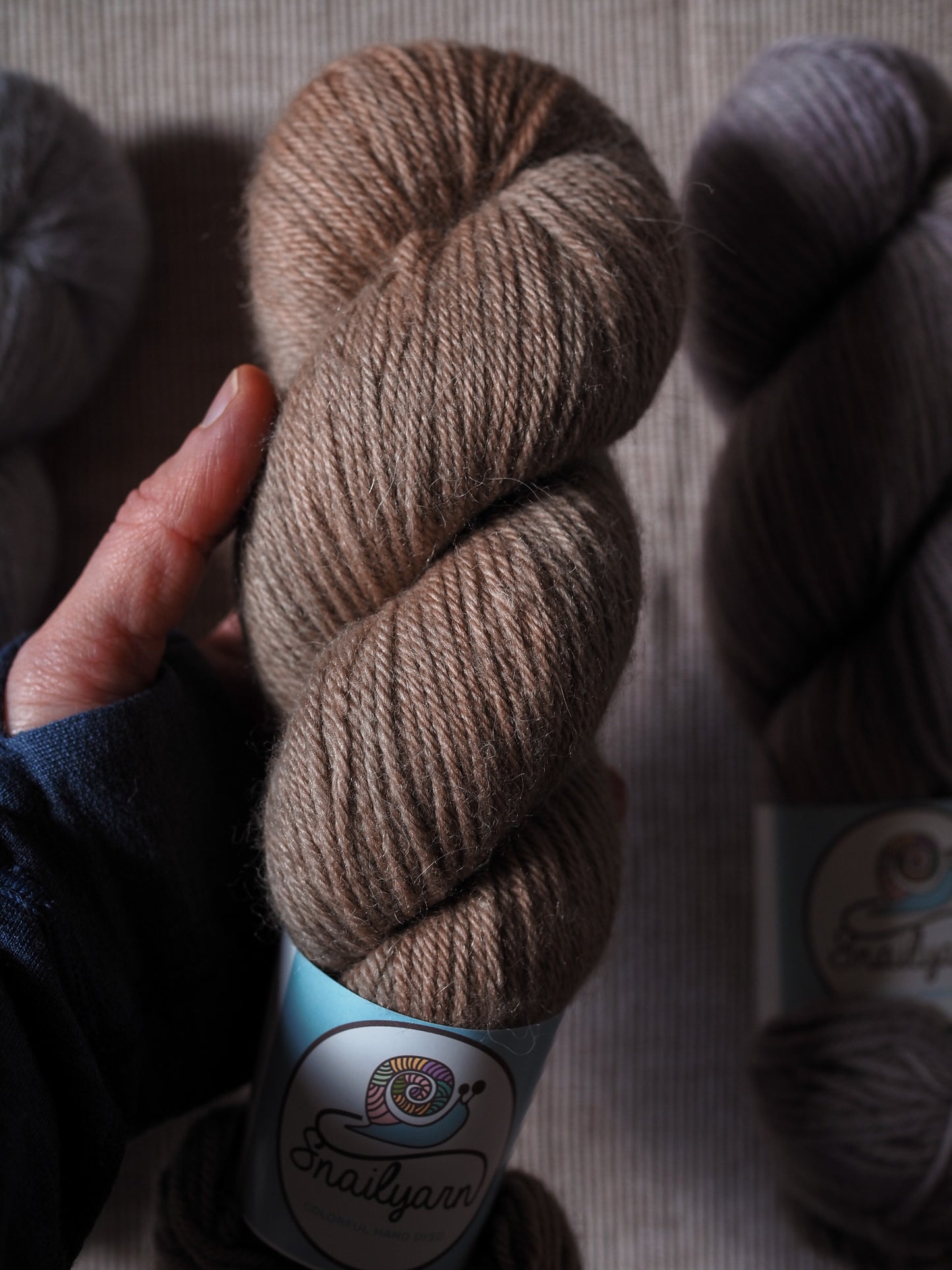 Brown skein of yarn held by a hand with a visible brand label on a neutral background