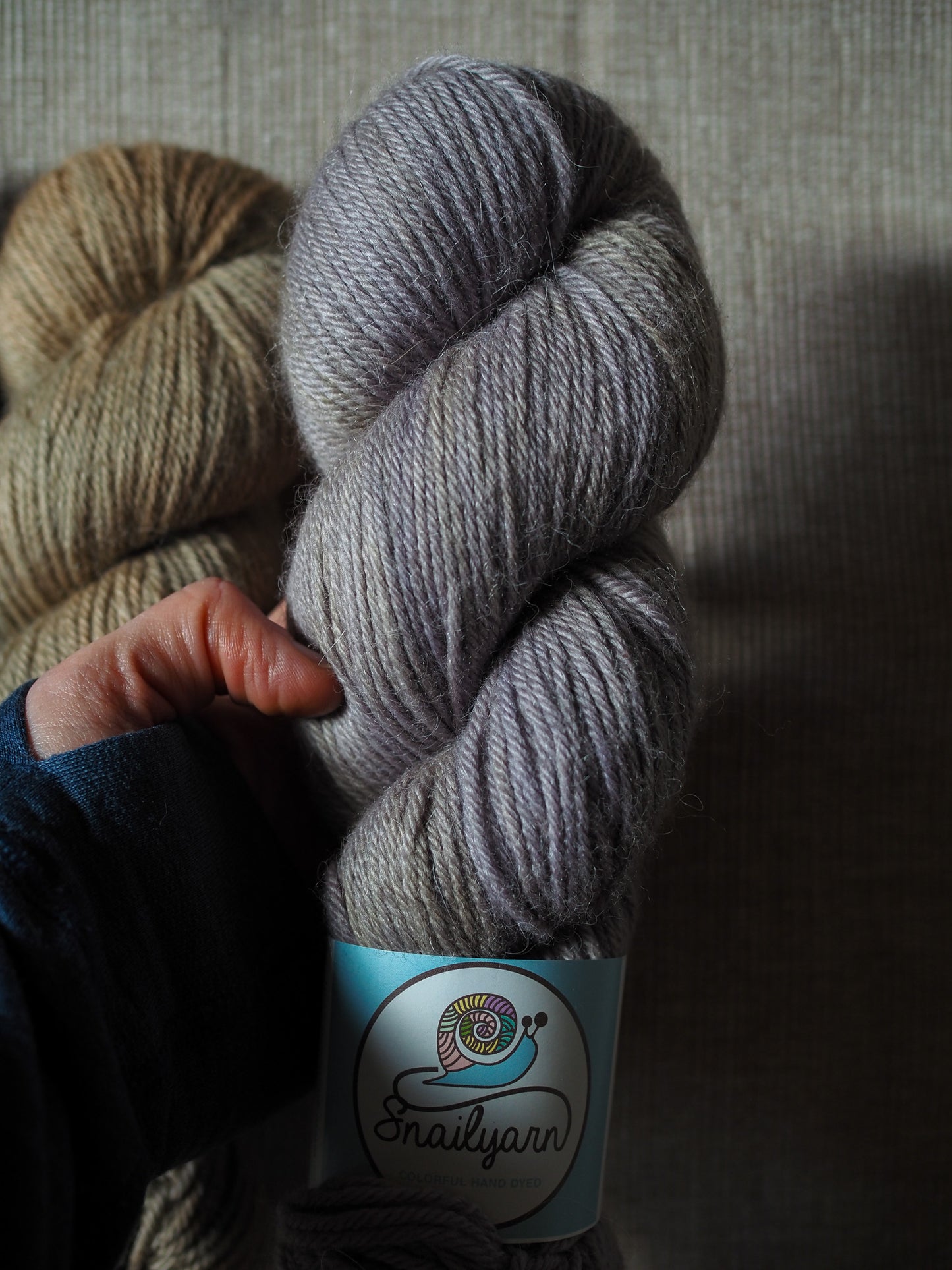 Gray skein of yarn held by a hand with a brand label on a neutral background