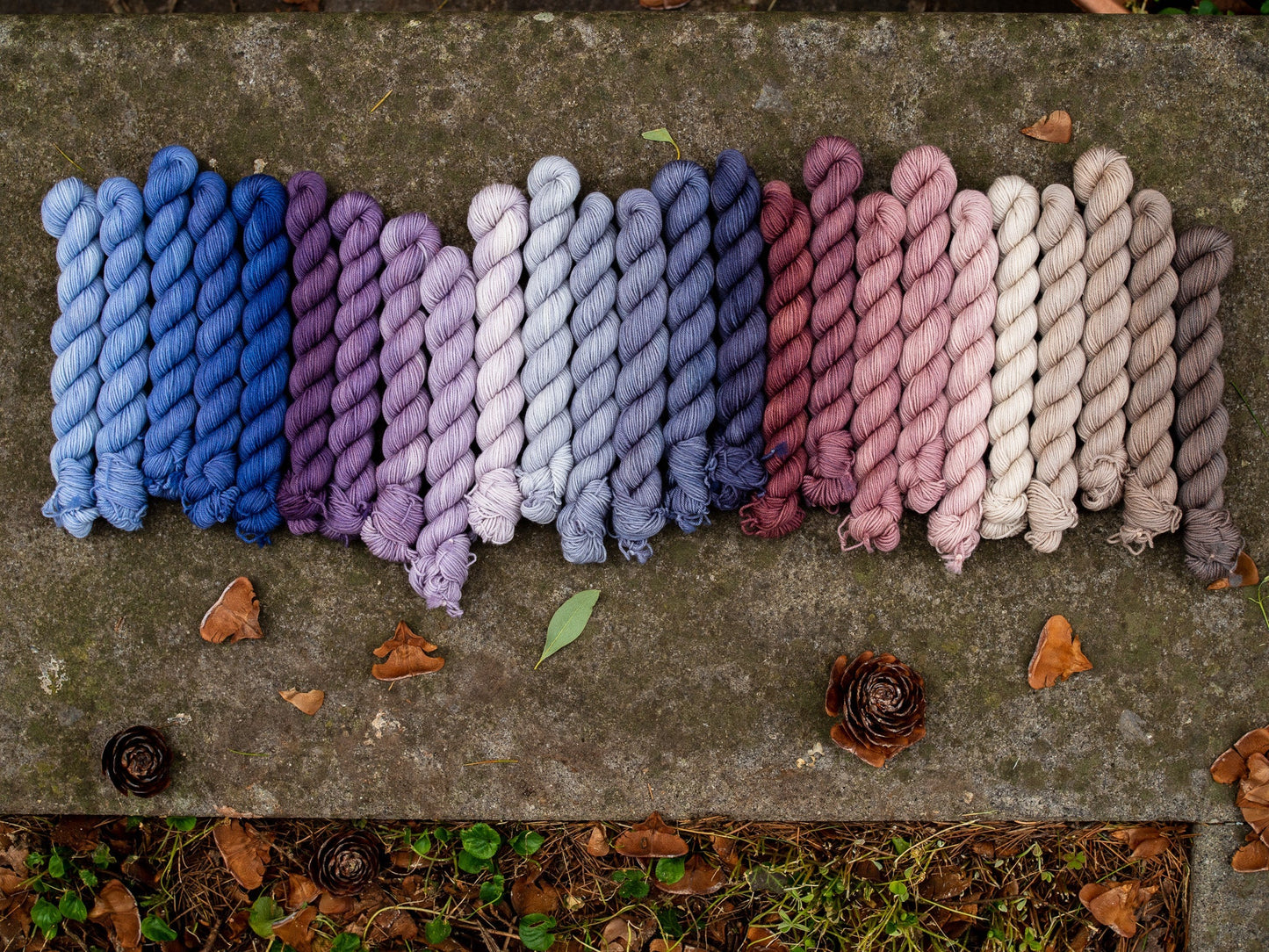 A line of hand dyed fade mini skeins of yarn in many colors arranged in a gradient.