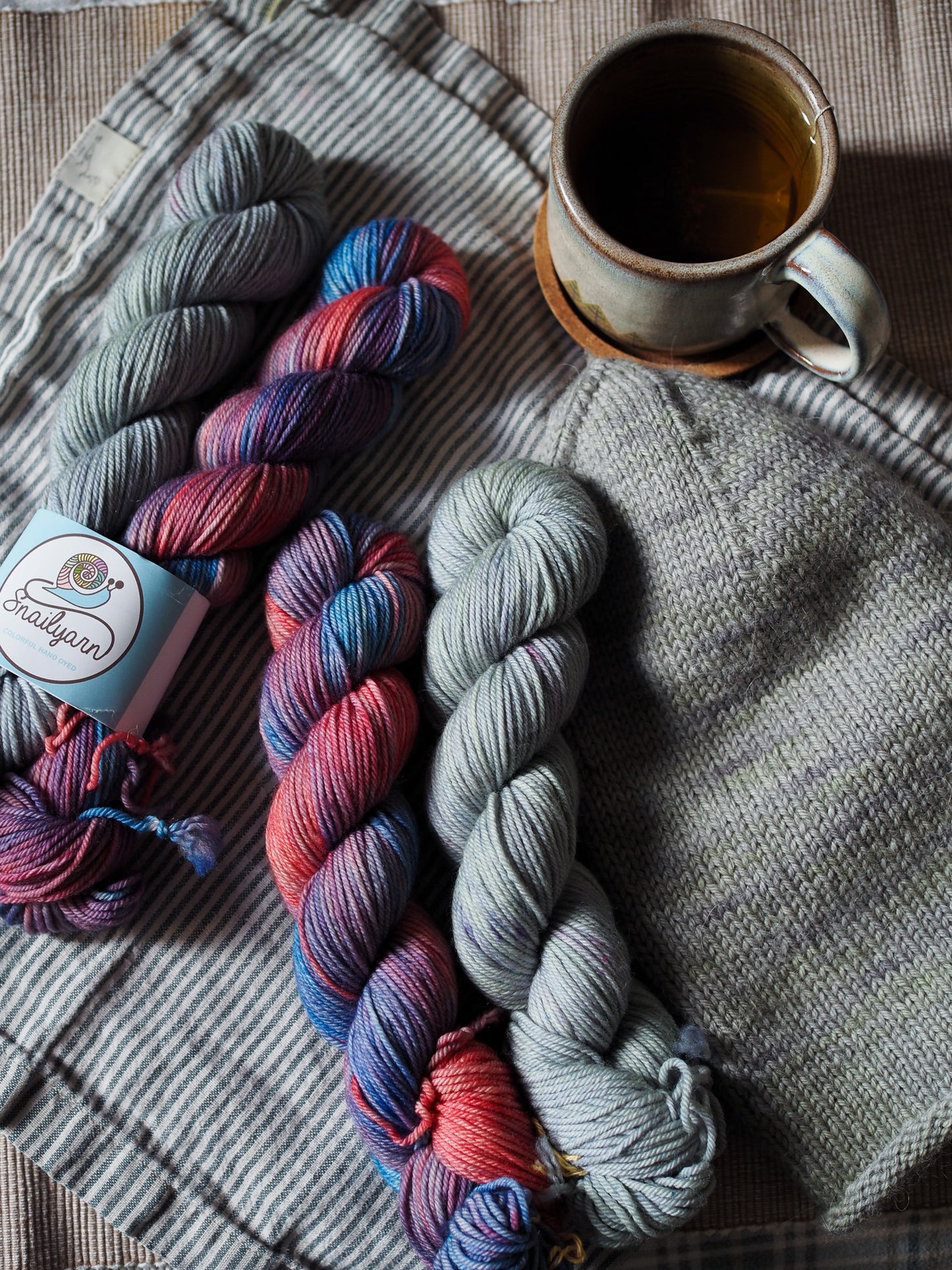 Three skeins of multicolored yarn on a textured fabric surface with a cup of tea.