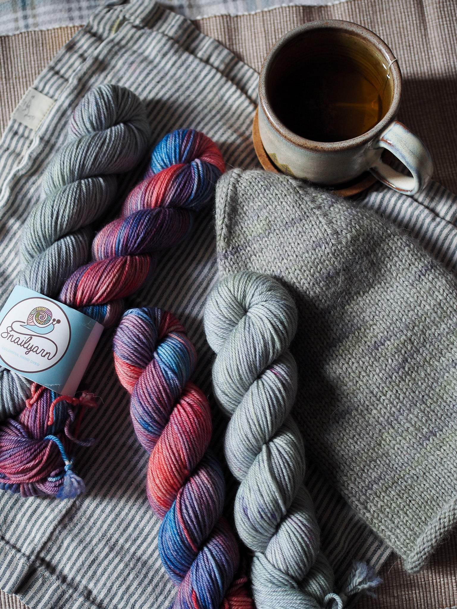 Two skeins of multicolored yarn and a cup of tea on a textured surface.
