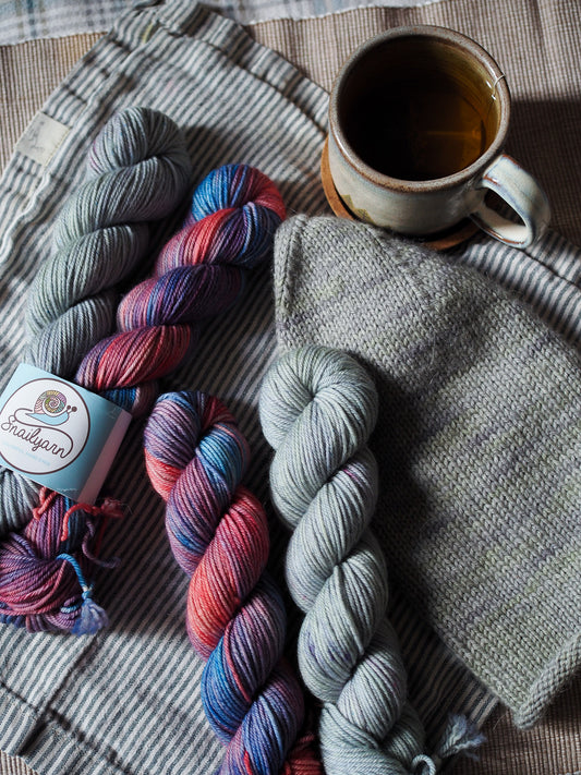 Two skeins of multicolored yarn and a cup of tea on a textured surface.